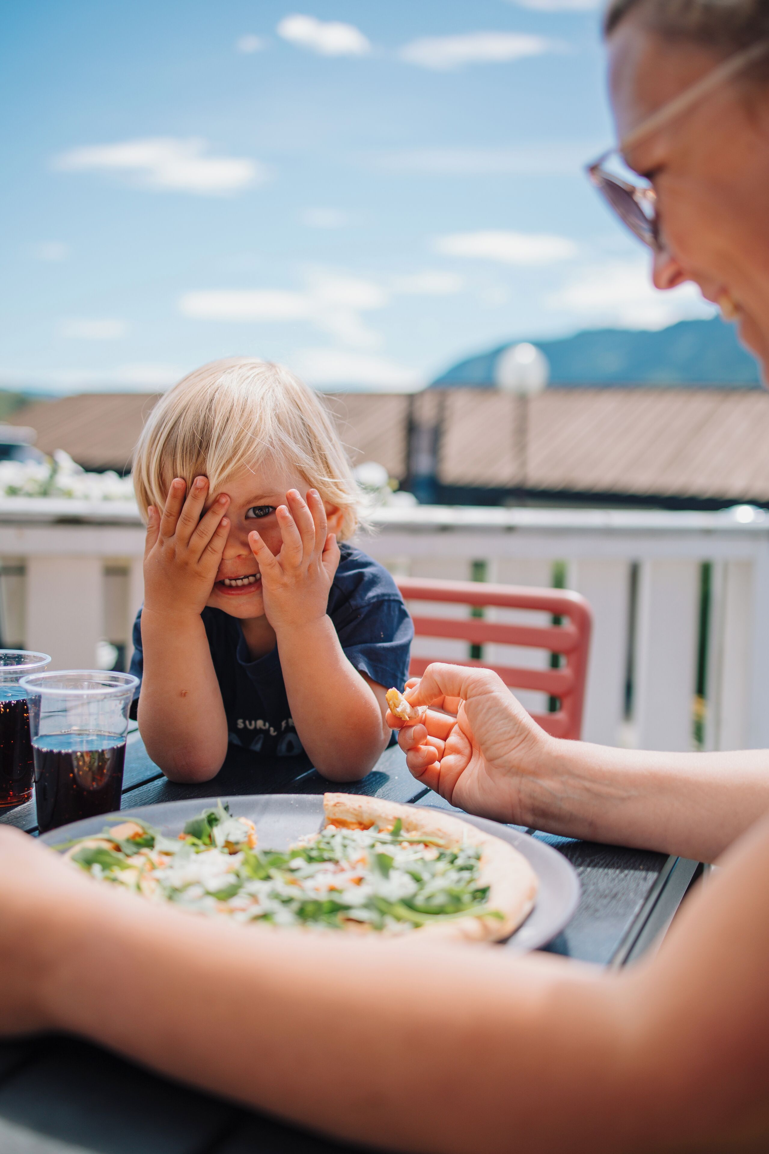 A dining table with a pizza and drinks, a red chair, and a person holding a piece of food.