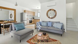 A modern living room with a grey sofa, a dining table with chairs, a kitchen area, and a staircase. - Selinofos - a modern seaside home blending comfort and sea views. (Naxos)