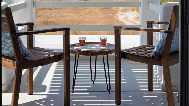 A balcony with two wooden chairs and a small table, overlooking a beach and the sea. - Selinofos - a modern seaside home blending comfort and sea views. (Naxos)
