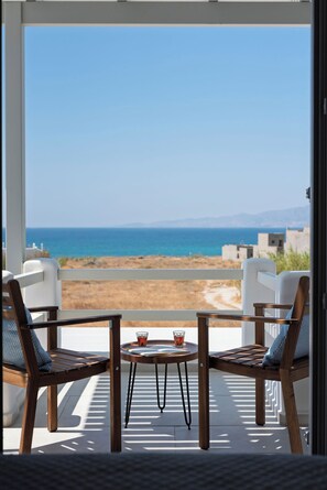 A balcony with two wooden chairs and a small table, overlooking a beach and the sea. - Selinofos - a modern seaside home blending comfort and sea views. (Naxos)
