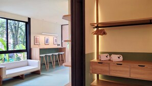 A modern hotel room with a large window, a wooden bench, a small kitchen area with stools, and a wooden cabinet with towels. - w Beautiful 1BR w Terrace in Poblado (Medellín)
