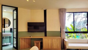 A modern hotel room with a large window, a flat-screen TV, a wooden desk, a sofa, and a bathroom visible through an open door. - w Beautiful 1BR w Terrace in Poblado (Medellín)