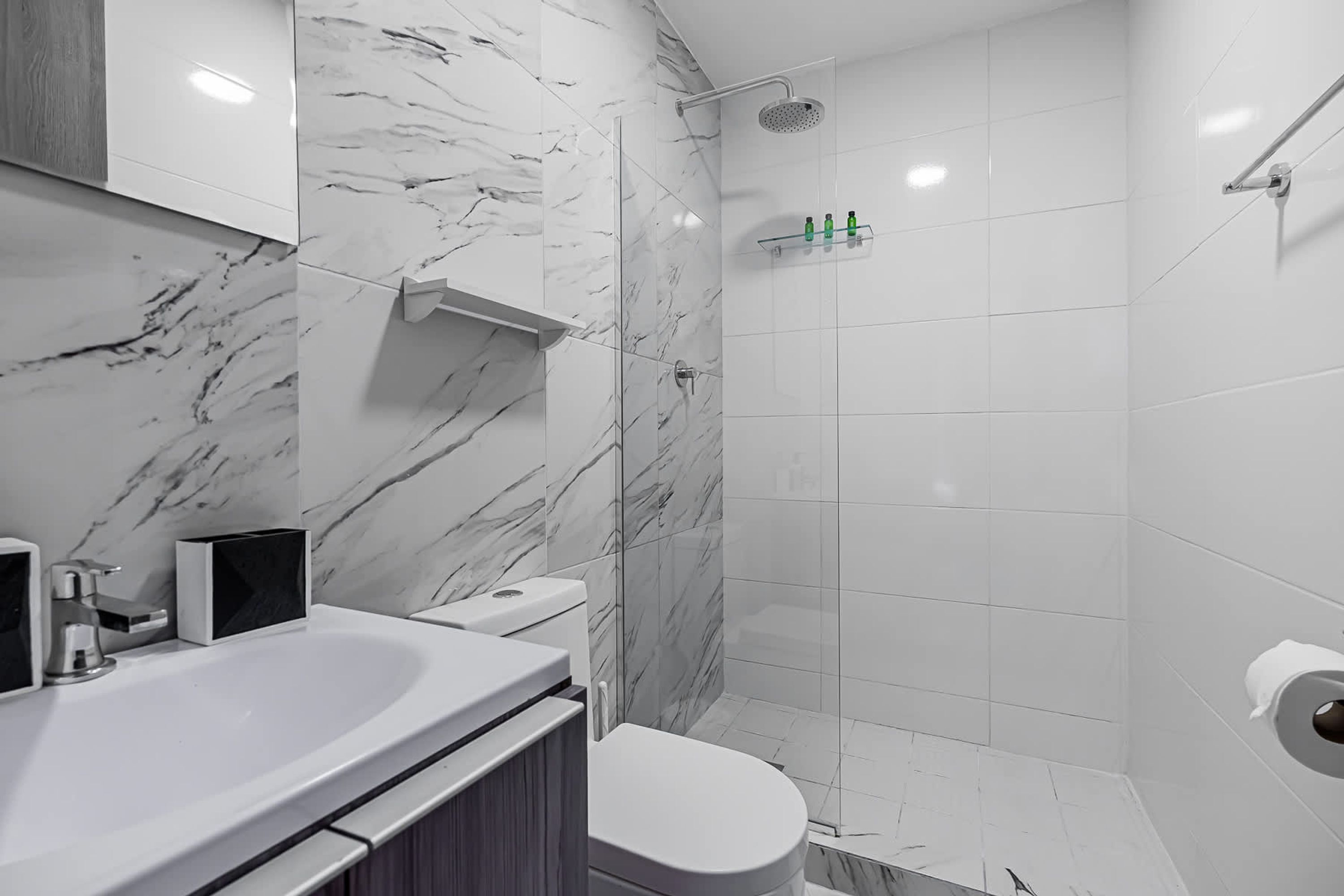 Une salle de bain moderne avec un pare-baignoire en marbre, une douche en verre et un lavabo blanc avec un miroir.