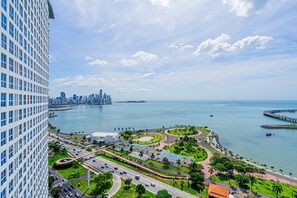 Een hoog hotel met uitzicht op een kustplaats, met een jachthaven, wegen en groen.