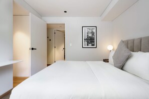A bedroom with a bed, a nightstand, a bedside lamp, a framed picture on the wall, and an open door leading to another room. - w Radiant 2BR in Roma Norte (Mexico City)