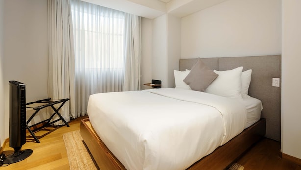 A modern hotel room with a large bed, a flat-screen TV, and a window with sheer curtains. - w Awesome 2BR in Roma Norte (Mexico City)