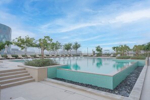 A rectangular swimming pool with a tiled edge, surrounded by lounge chairs and small trees. - Stayshort - Cozy 1BR Apartment Located in Dubai Hills (Dubai)