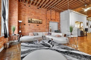 A spacious living area with a brick wall, white sofa, and a modern coffee table. - New! Huge Downtown Loft - Game Room - Free Parking (Detroit)