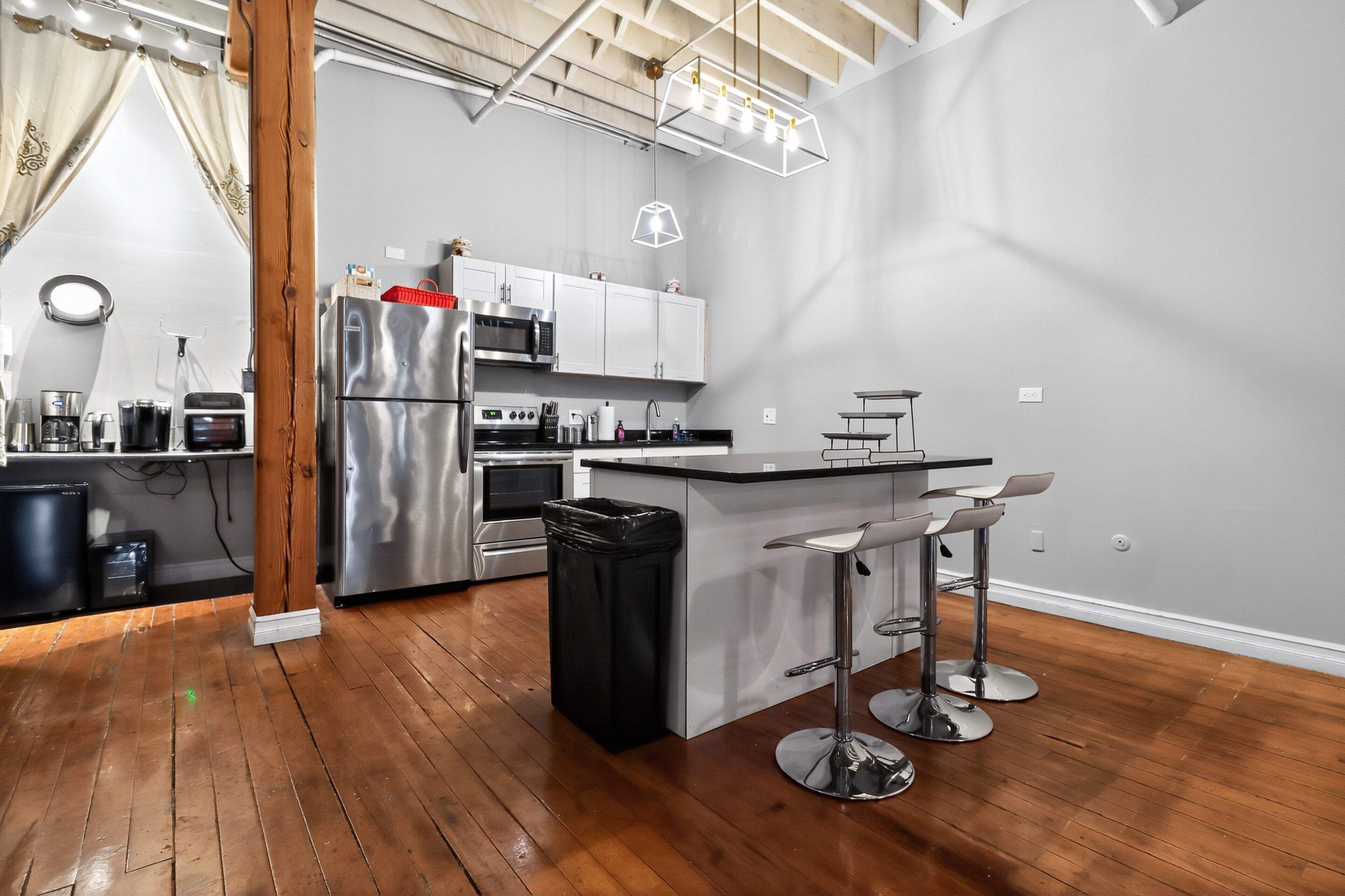 A modern kitchen with stainless steel appliances, a wooden floor, and a bar area with stools.