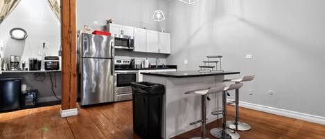 A modern kitchen with stainless steel appliances, a wooden floor, and a bar area with stools.
