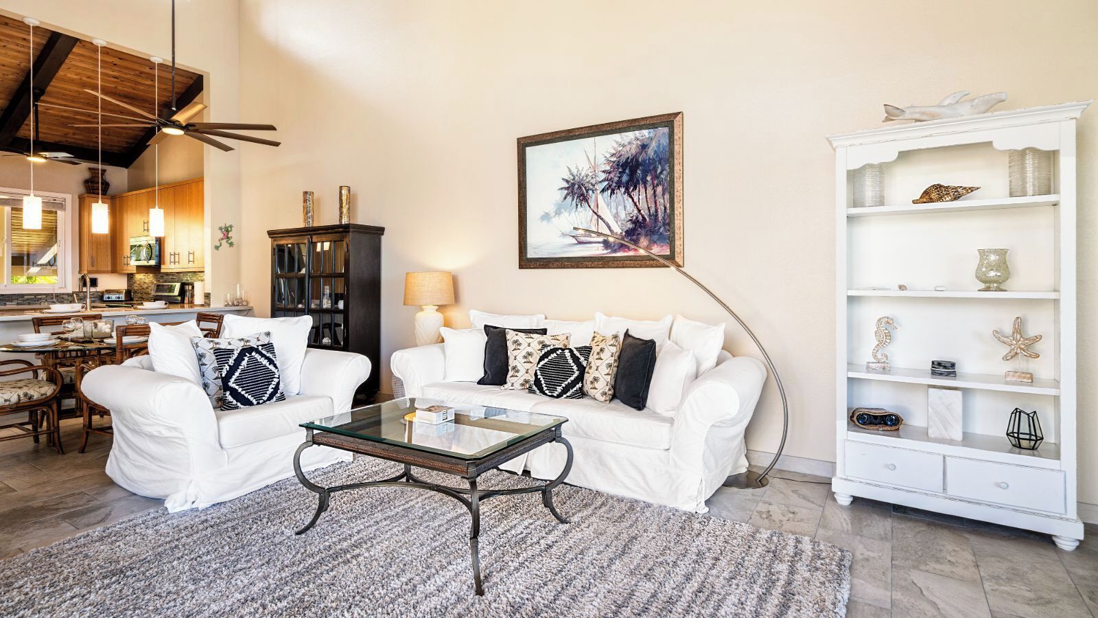 A living room with a white sofa set, a glass coffee table, and a white sideboard with decorative items.