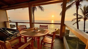 A wooden table with chairs on a balcony overlooking the ocean at sunset. - Oceanfront Corner Penthouse with Sunset Views, Partial A/C, and Wraparound Lanai (Kailua-Kona)