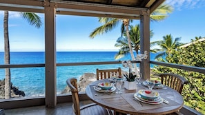 A table set for dining with a view of the ocean and palm trees. - Oceanfront Corner Penthouse with Sunset Views, Partial A/C, and Wraparound Lanai (Kailua-Kona)