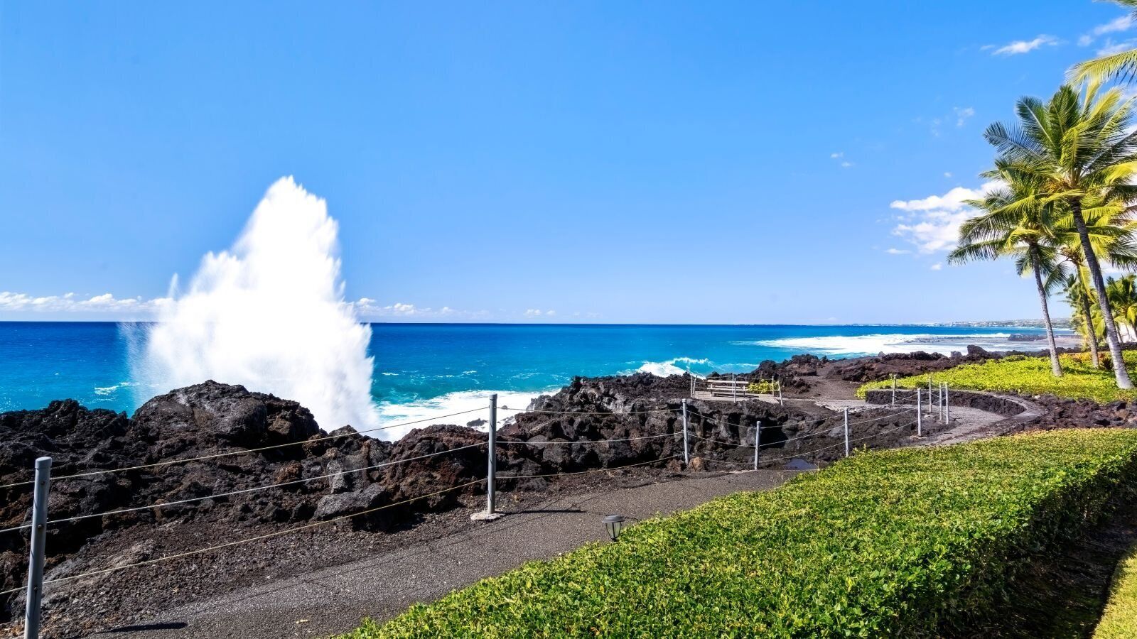A coastal landscape with a rocky shoreline, a clear blue sky, and a view of the ocean.