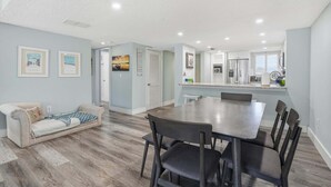 A modern living room with a sofa, dining table, and chairs. There is a kitchen area with a refrigerator and cabinets. - Oceanfront Condo, Pool Access & Private Patio (St. Augustine)