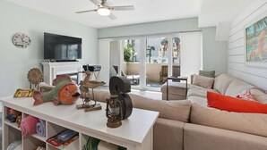 A living room with a flat-screen TV, a ceiling fan, a fish decoration, a lantern, and a sofa with orange pillows. - Oceanfront Condo, Pool Access & Private Patio (St. Augustine)