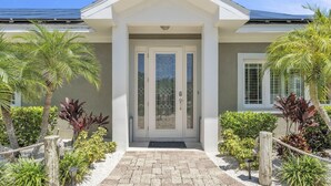 Une maison moderne à la façade symétrique, dotée d’une entrée centrale avec une porte vitrée et d’une allée pavée.
