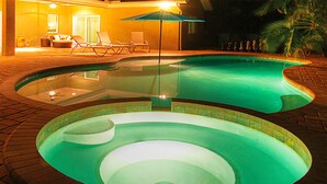 Une piscine au design original, entourée de chaises longues et agrémentée d’un parasol.