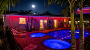 Un área de piscina con dos jacuzzis, una pared iluminada en rojo y una puerta que da a un porche cubierto.