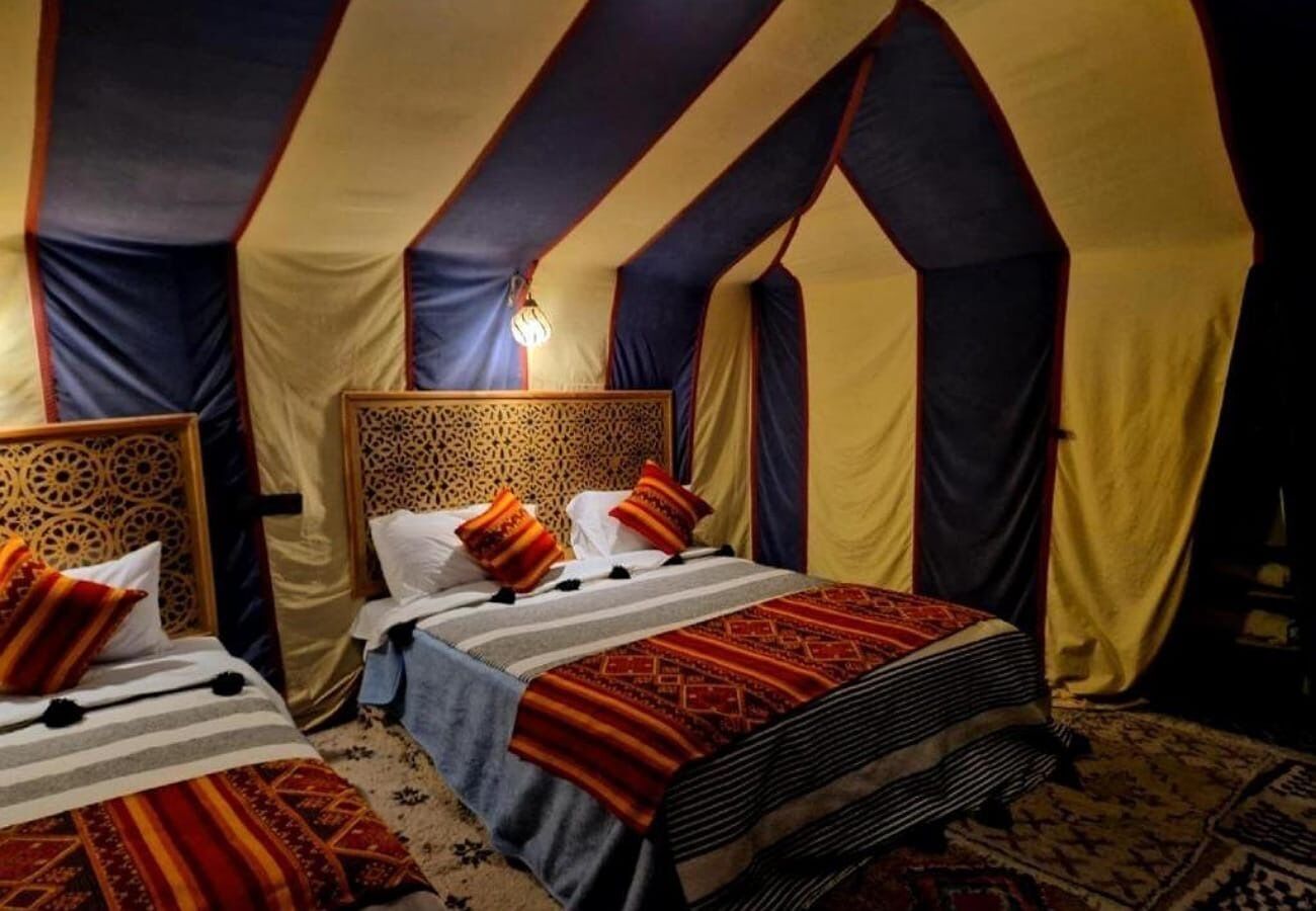 Habitación tipo tienda con dos camas, cada una con ropa de cama estampada y cabeceros.