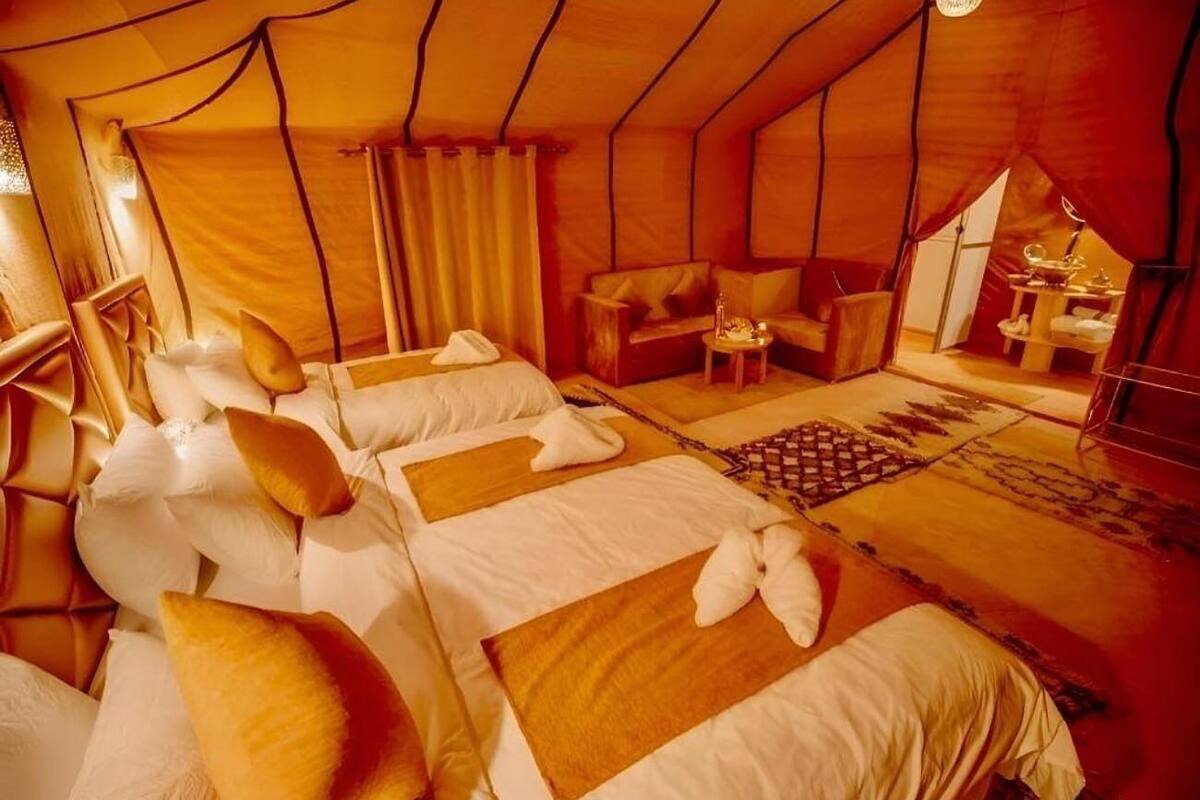 A tent-style room with three beds, each with pillows and towels. There is a small table with a lamp and a decorative item.