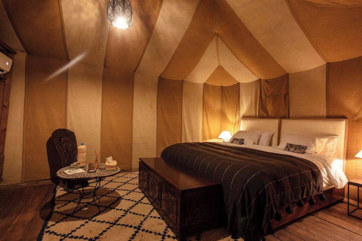 A tent-style room with a bed, bedside table, and a small round table with a chair.