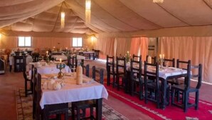 A tented dining area with tables set for service, chandeliers hanging from the ceiling, and a red carpet leading to the entrance. - Lantern Luxury Camp (Merzouga)