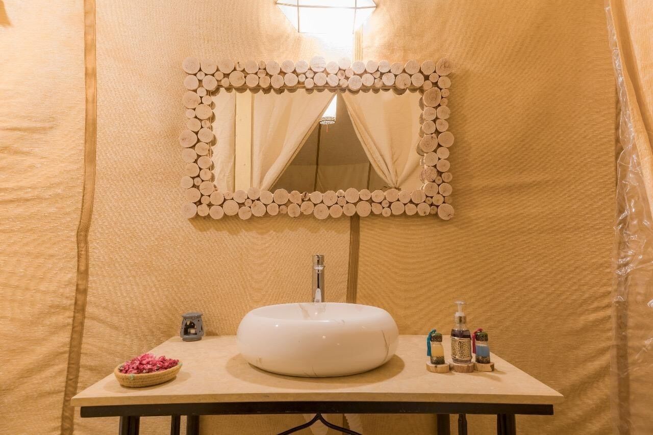 Un baño con un lavamanos redondo, un espejo con marco de madera y artículos de aseo en la encimera.