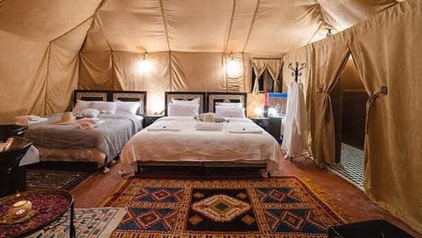 A tent-style bedroom with two beds, a patterned rug, and a chandelier. - Lantern Luxury Camp (Merzouga)
