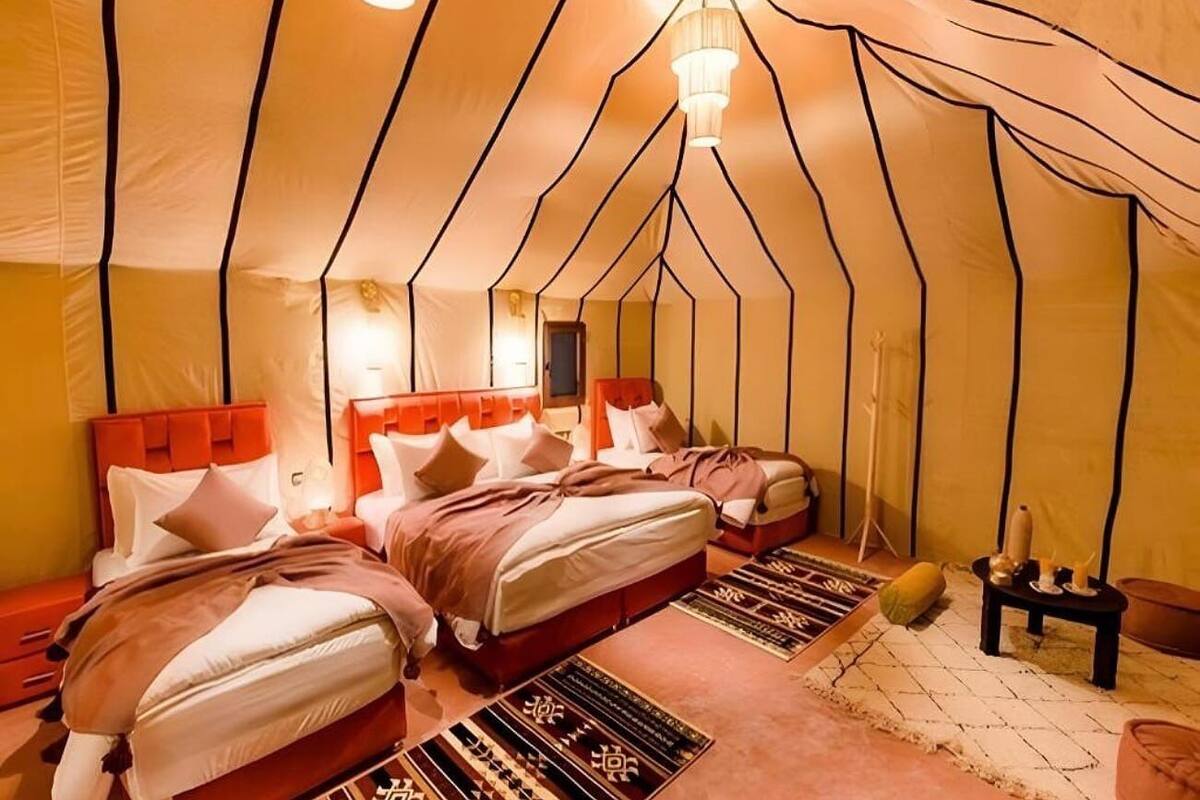 A tent-style room with two beds, a small table, and a lamp.