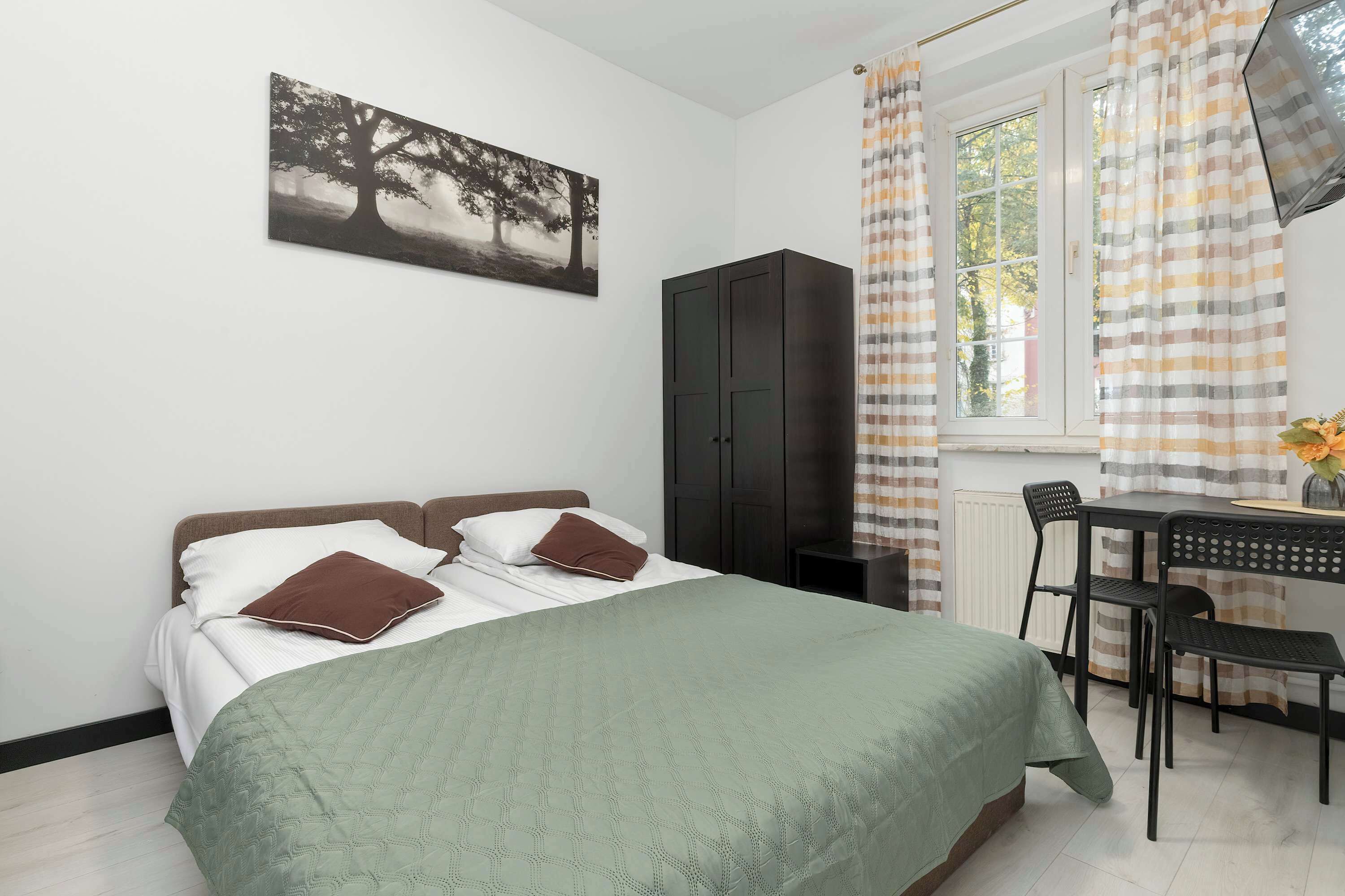 Un dormitorio con cama, escritorio, silla, armario y ventana con cortinas.