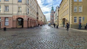 Eine Kopfsteinpflasterstraße, gesäumt von historischen Gebäuden, darunter ein markanter Turm mit einer grünen Turmspitze.
