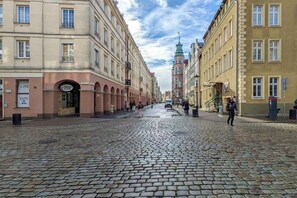 En kullerstensgata kantad av historiska byggnader, inklusive ett framstående torn med en grön spira.