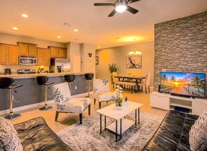 A modern living room with a flat-screen TV, leather sofas, a coffee table, and a dining area with a table and chairs. - Renovated 4BR Paradise Palms Resort Pool Townhome near Disney (Kissimmee)