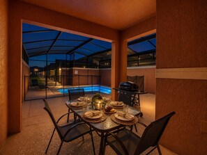 An outdoor dining area with a glass-enclosed pool, a barbecue grill, and a table set for two. - Renovated 4BR Paradise Palms Resort Pool Townhome near Disney (Kissimmee)