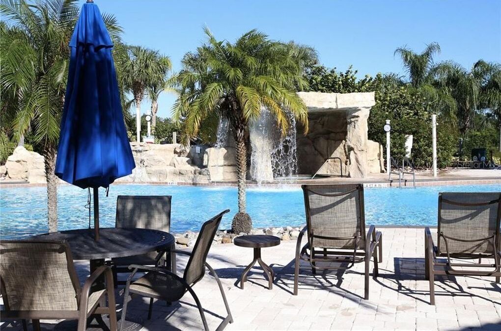 A poolside area with lounge chairs, a blue umbrella, and a waterfall feature.