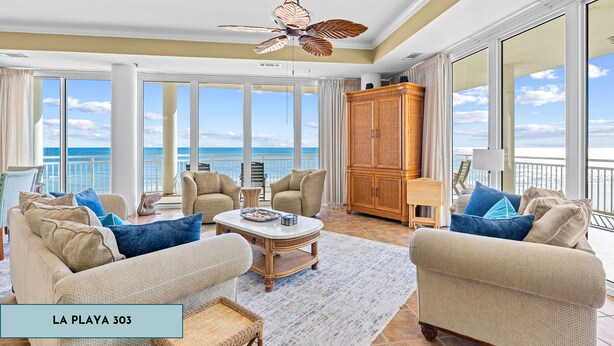 Uma sala de estar ampla com vista para o oceano, equipada com sofás bege, uma mesa de centro e um armário de madeira.