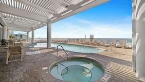 A covered pool area with lounge chairs and a hot tub, overlooking a beach. - The Colonnades 701 by Liquid Life (Gulf Shores)