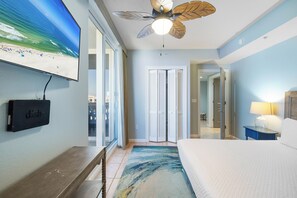 Ein Schlafzimmer mit Bett, Deckenventilator, Fernseher und Blick auf den Strand durch das Fenster.