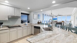 A modern kitchen with white cabinetry, a marble countertop, and a view of the ocean through large windows. - The Colonnades 701 by Liquid Life (Gulf Shores)