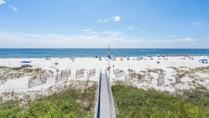A beach with a wooden boardwalk leading to the shore, sandy beach, and umbrellas. - The Colonnades 701 by Liquid Life (Gulf Shores)
