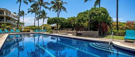 A swimming pool with clear blue water, surrounded by palm trees and lounge chairs.