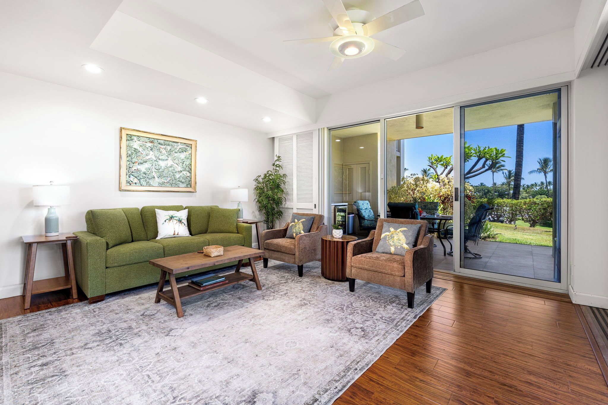 A modern living room with a green sofa, two armchairs, a coffee table, and a large sliding glass door leading to a garden.