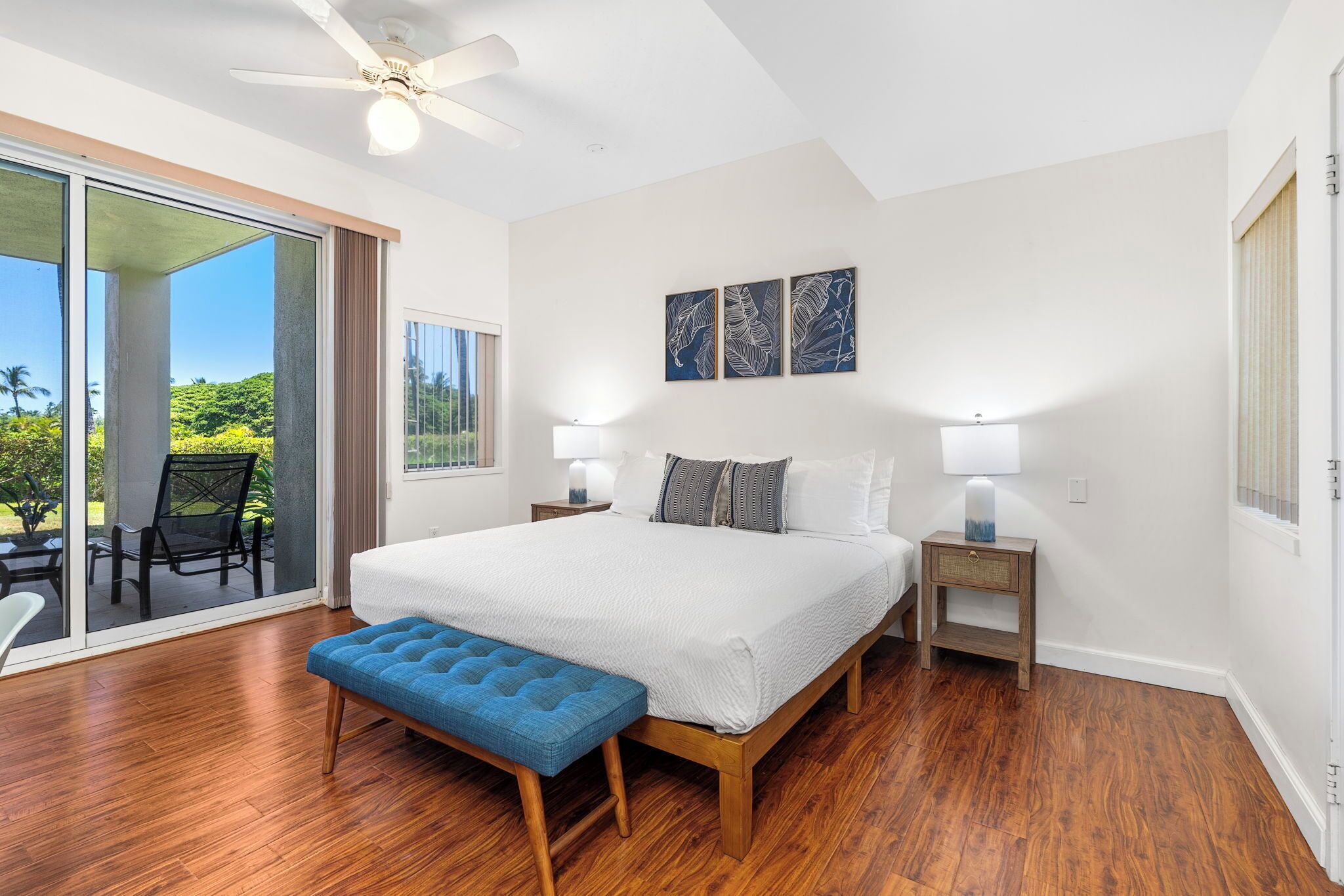 Une chambre dotée d’un grand lit, d’un ventilateur de plafond et offrant une vue sur la verdure grâce à une porte-fenêtre coulissante.