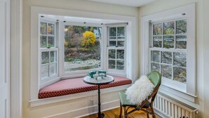 Une pièce d’angle avec une baie vitrée, une table avec un banc rembourré de coussins rouges et une chaise avec un coussin blanc.