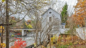Une maison située près d’une rivière, avec un pont et un paysage automnal.