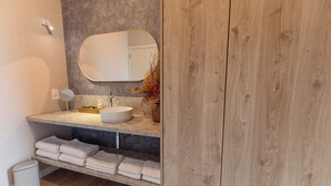 Un bagno moderno con uno specchio rotondo, un lavabo bianco e asciugamani ordinatamente piegati su uno scaffale.