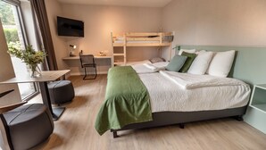 Una moderna camera d'albergo con un letto a castello, una scrivania con una sedia, una TV a parete e una finestra con tende.