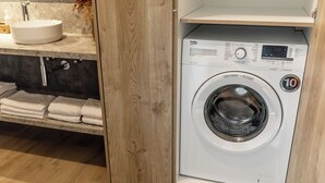 Una lavanderia piccola e moderna, con lavatrice integrata, lavandino e asciugamani riposti ordinatamente su uno scaffale.
