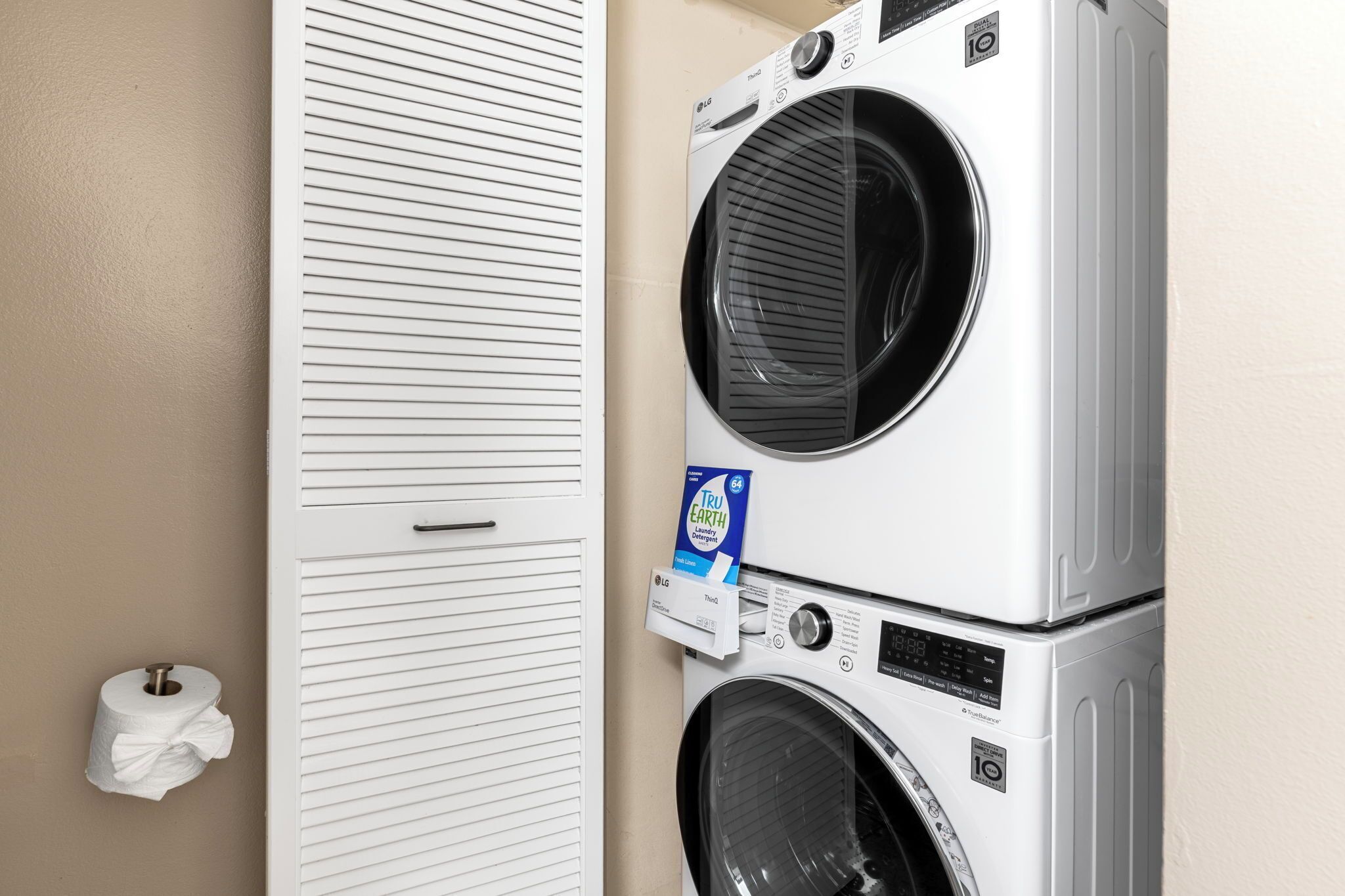 Un espace buanderie comprenant deux machines à laver superposées et un porte-rouleau de papier toilette.